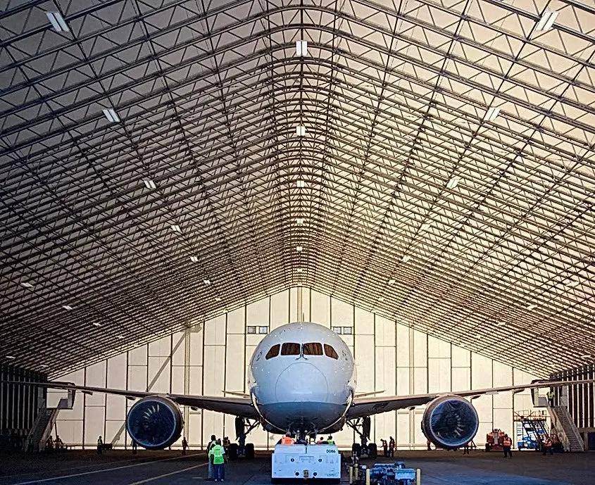 Wide-body aircraft beneath the clear-span steel trusses of a tension-fabric hangar at Robins Air Force Base