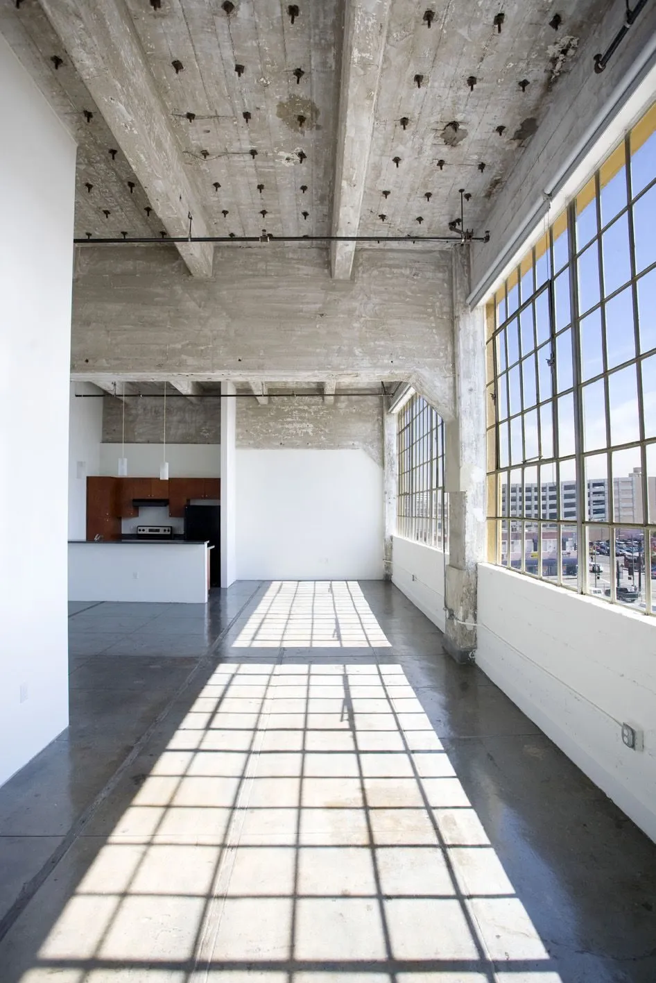 Empty Santee Court loft with exposed concrete waffle ceiling, polished concrete floor, and tall steel-grid windows
