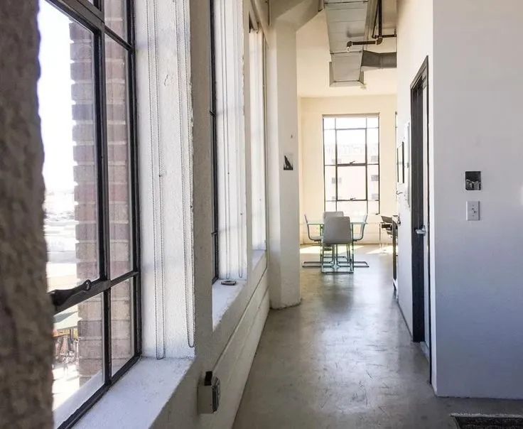 Santee Court loft interior with floor-to-ceiling steel-framed windows, exposed ductwork, and a sunlit dining area