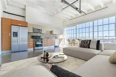Furnished Santee Court loft living room and open kitchen below exposed painted ceiling pipes, with city-view windows