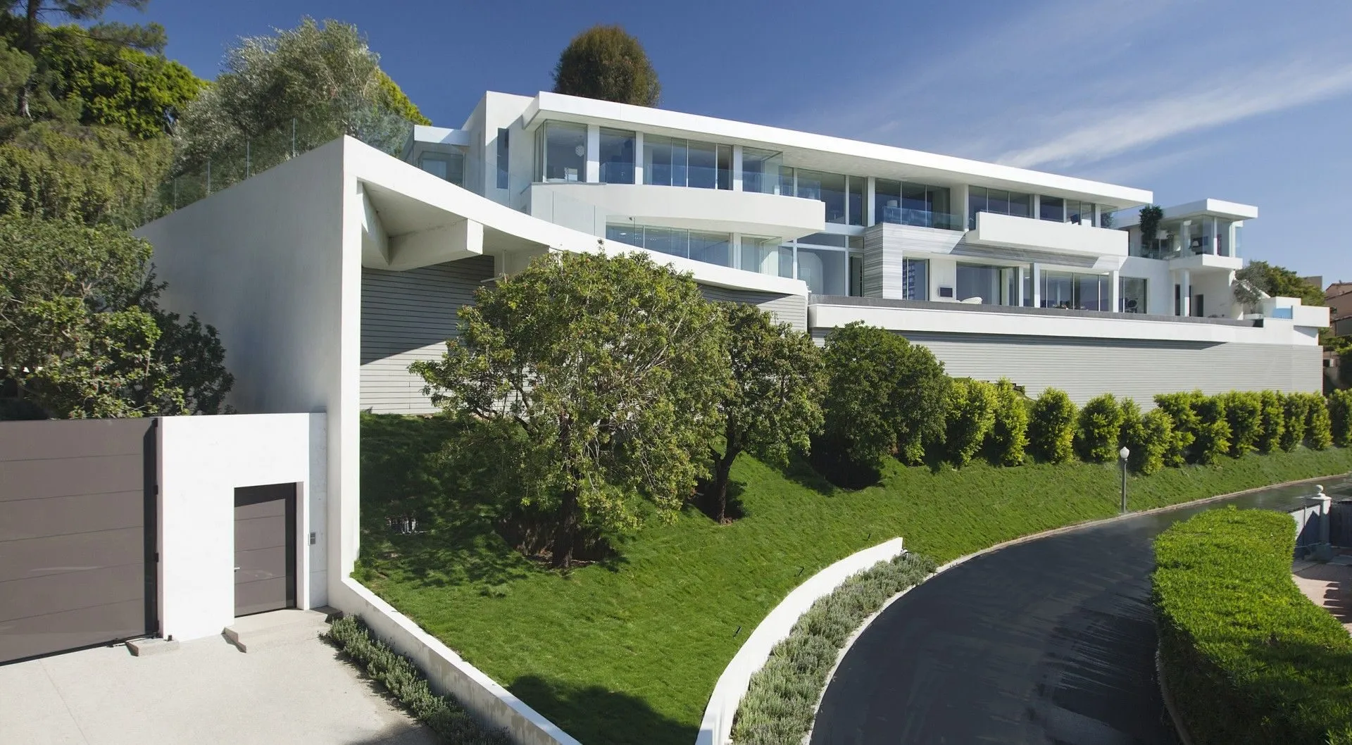 White hillside residence above a curved driveway and lawn