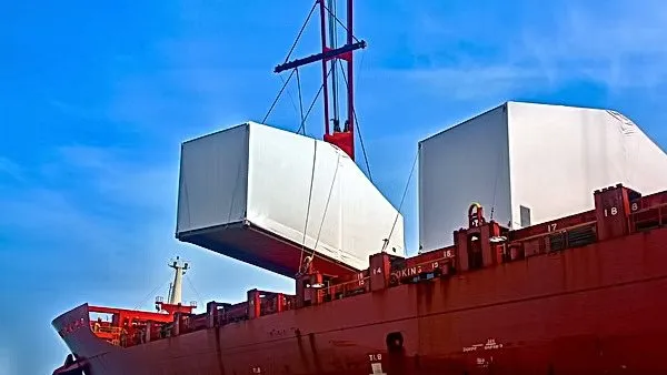 Crane lifting a tension-fabric warehouse module from the deck of a cargo ship