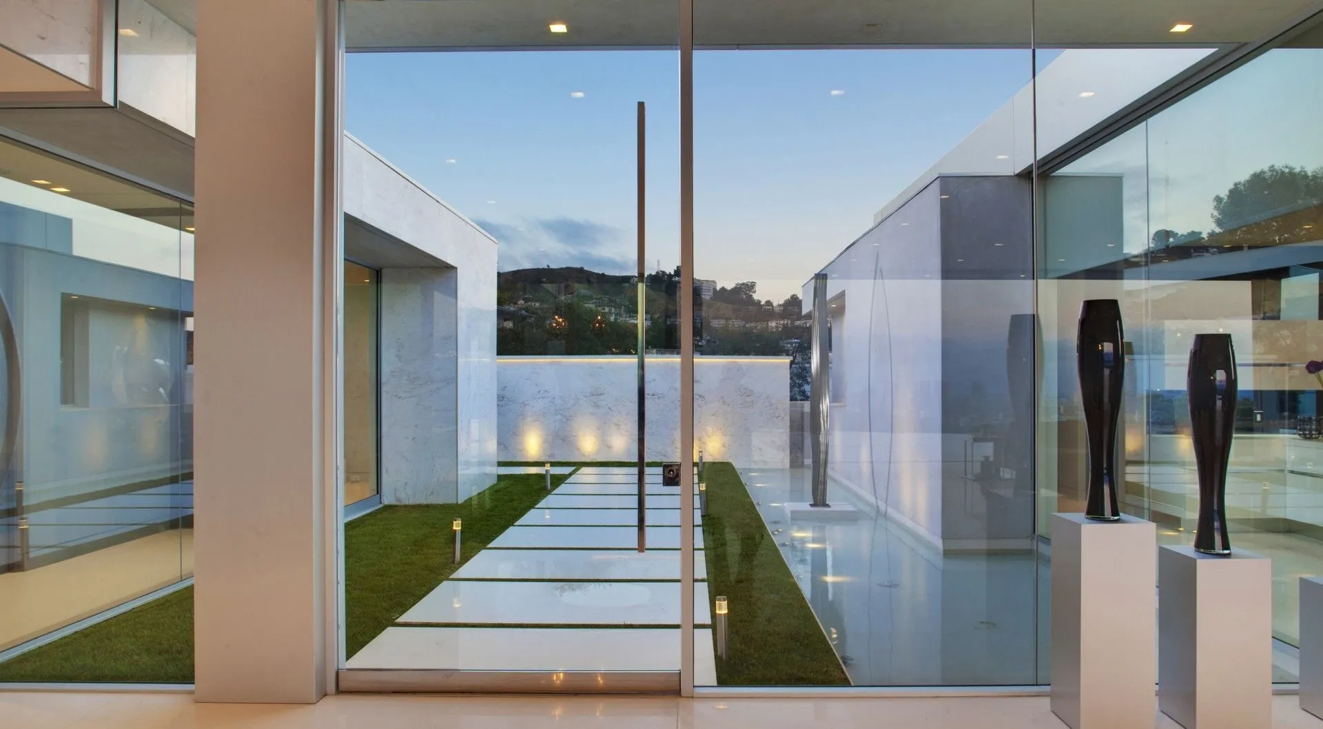 Glass-walled entry corridor with sculpture and courtyard water